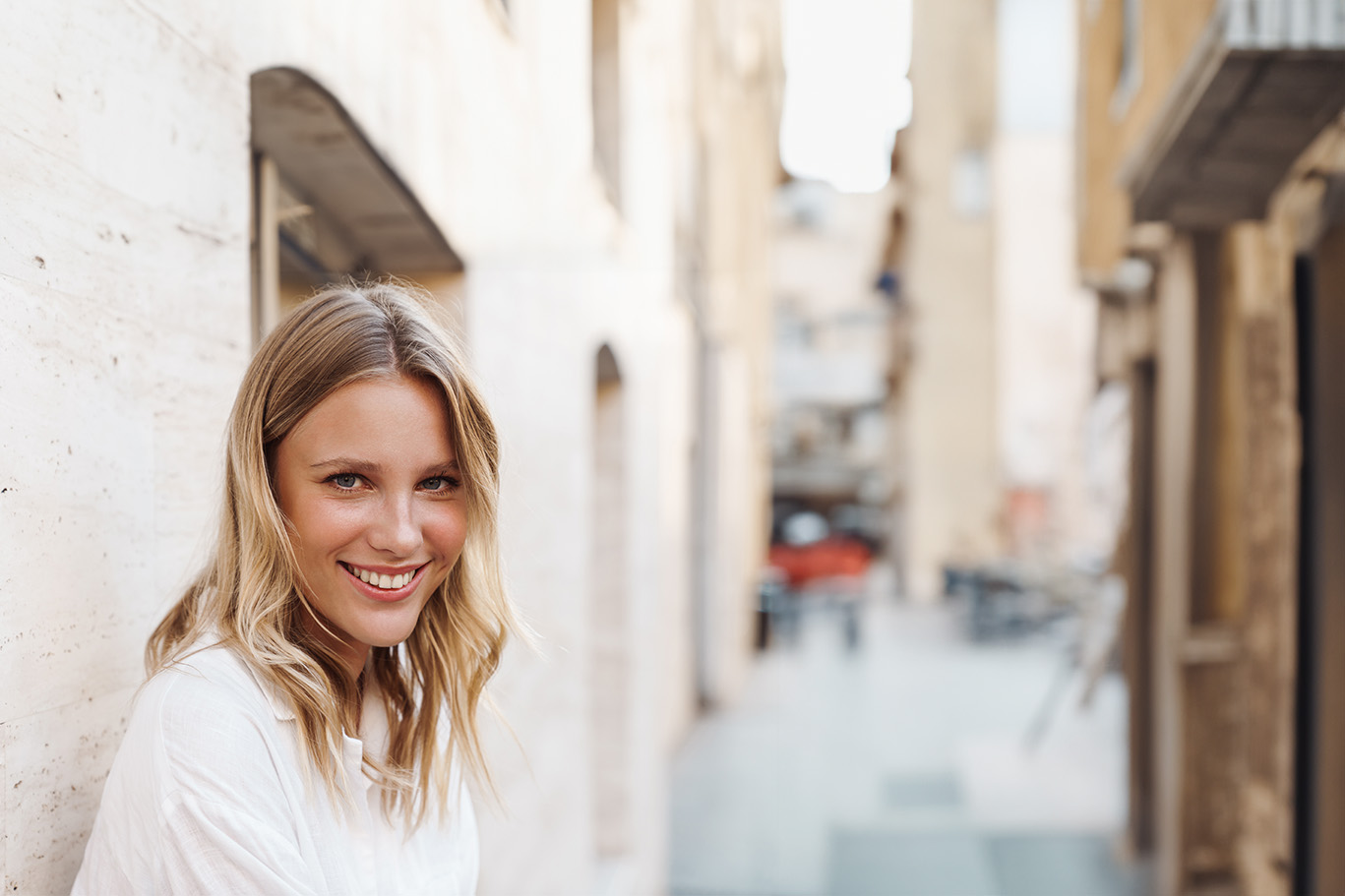 A woman poses against a rustic background with exposed brick walls and wooden beams.